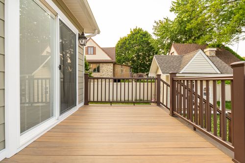 Wood deck corner with sliding glass door and dark railings overlooking a neighboring stone house
