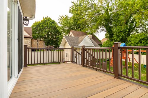 Wood deck with dark railings overlooking a detached garage and neighboring homes