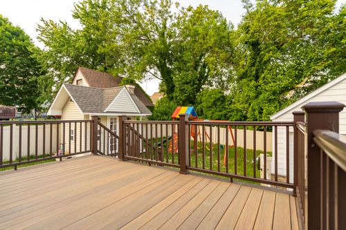 Wood deck railing overlooking a backyard playset and detached white garage