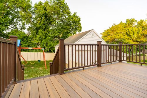Deck corner overlooking a backyard swing set and lawn shaded by mature trees