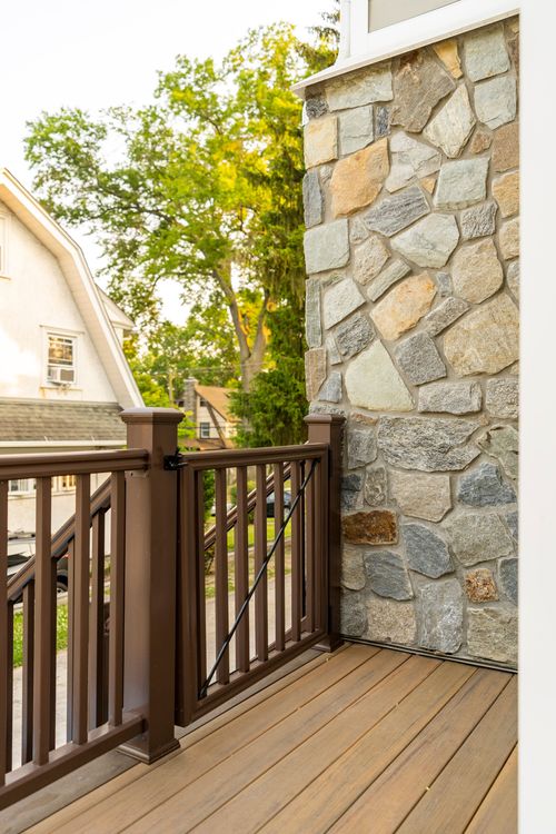 Deck corner detail showing a stone-clad wall beside dark wood railings and a gate