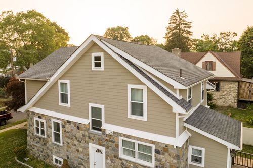 Aerial view of a tan two-story home with stone base and gray shingle roof at golden hour