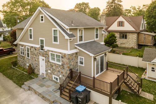 Aerial view of a stone-and-siding home with new sunroom addition and multi-level wood deck