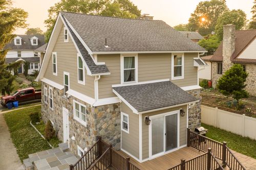 Aerial view of a craftsman-style home with gable roof and rear deck addition at sunset