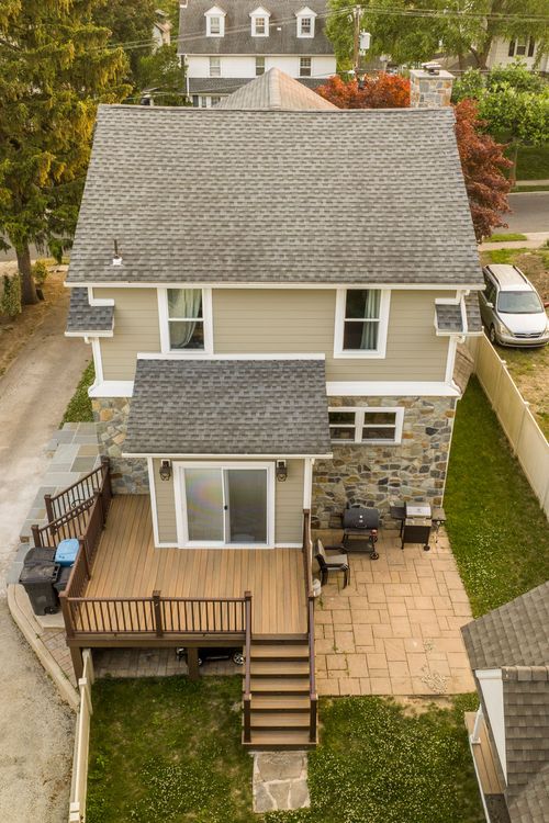Aerial top-down view of a wood deck and stone patio with grill behind a stone-and-siding home