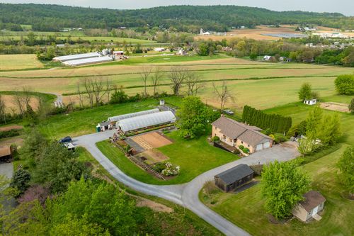 Aerial view of a farmhouse property with greenhouse, outbuilding and rolling green fields