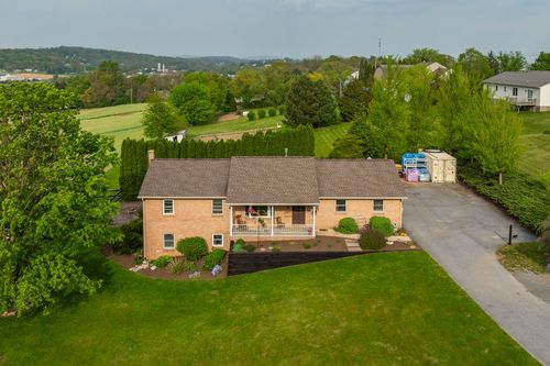 Aerial view of a brick ranch home with covered porch and gravel driveway near a nursery
