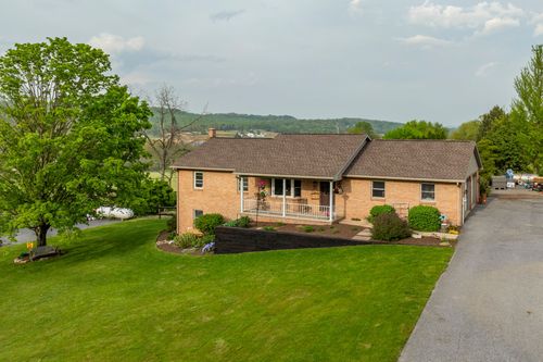 Aerial view of a brick ranch home surrounded by mature shade trees and open lawn