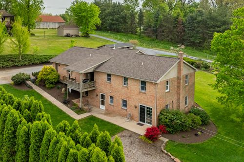 Aerial view of a two-story brick home with rear deck, stone chimney and manicured landscaping