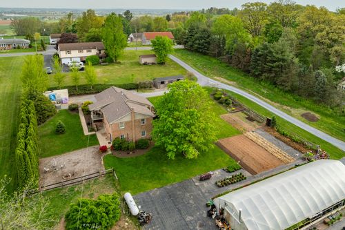 Aerial view of a brick home with detached garage, mature shade tree and garden beds