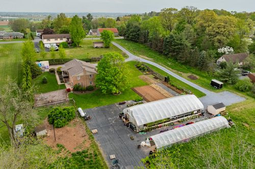Aerial view of a greenhouse nursery with rows of potted plants beside a brick home