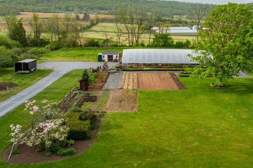 Aerial view of a hoop-house greenhouse with cultivated garden rows and flowering shrubs