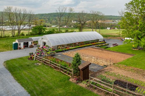 Aerial view of a greenhouse nursery stocked with flowering plants beside garden plots