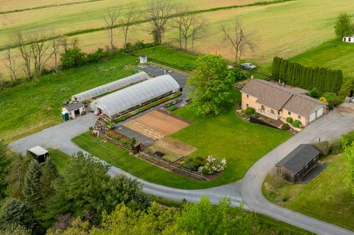 Aerial view of a brick ranch home with attached garage bordered by evergreen trees and open fields