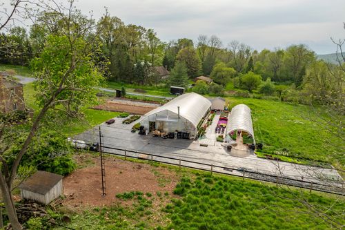 Aerial view of a hoop-house greenhouse and outdoor seating area bordered by lawn at dusk