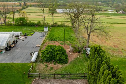 Aerial view of a gravel lot beside a greenhouse bordered by bare trees and a small hoop house