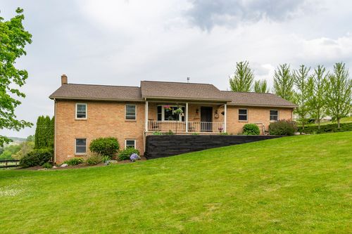 Rear elevation of a two-story brick home with wood deck, stone chimney and mature landscaping