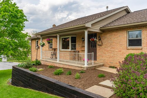 Gravel patio with outdoor seating bordered by a tall arborvitae hedge and red flowering shrubs