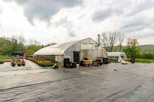 Hoop-house greenhouse exterior with tools and supplies stored along a gravel yard