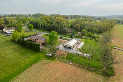 Aerial view of a hoop-house greenhouse and cultivated garden rows beside a brick home