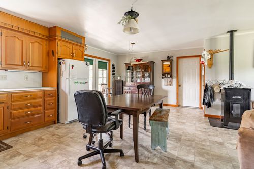 Kitchen with oak cabinetry and dining table, wood stove and coat hooks visible beyond