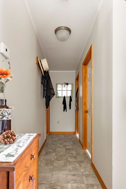 Narrow hallway with wood-trimmed doors, wall coat hooks and tile flooring
