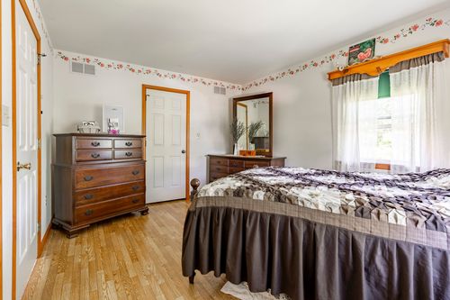 Bedroom with wood dresser, mirror and quilted bed beneath a floral wallpaper border