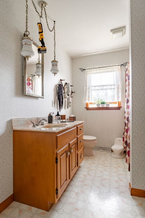 Bathroom with double pendant lighting, wood vanity and floral wallpaper