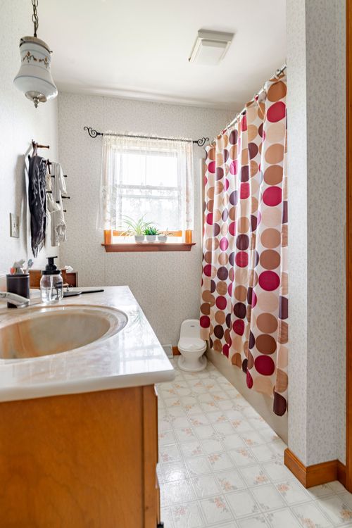 Bathroom with a polka-dot shower curtain, wood vanity and floral wallpaper