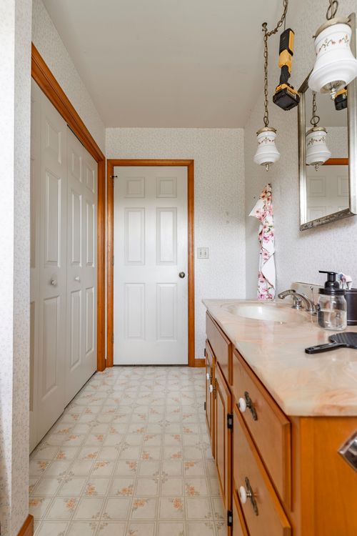 Bathroom hallway with double closet doors, a white panel door and wood vanity beneath globe pendant lights