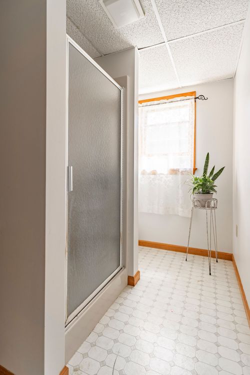 Bathroom nook with a frosted-glass shower stall and a lace-curtained window holding a potted plant