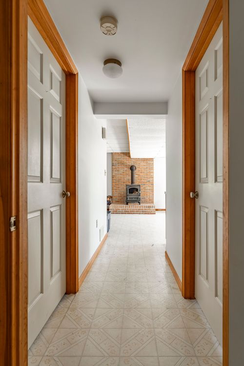Hallway with facing white paneled doors leading to a brick wood-stove fireplace beyond
