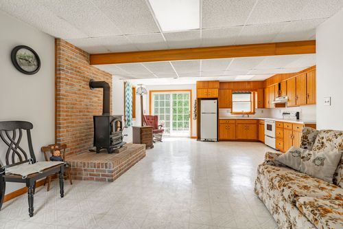 Open basement rec room with brick wood-stove surround and a kitchenette in the background