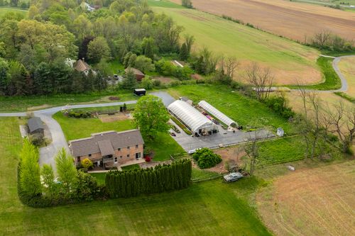 Aerial view of a greenhouse nursery beside a brick home with barn and open farmland beyond
