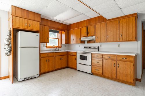 Basement kitchenette with wood cabinetry, white refrigerator and electric range