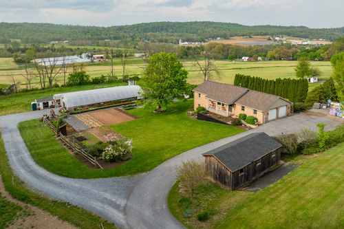Aerial view of a hoop-house greenhouse, potting shed and garden plots with rolling hills beyond