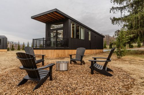 Four black Adirondack chairs around a fire pit with the tiny cabin in the background