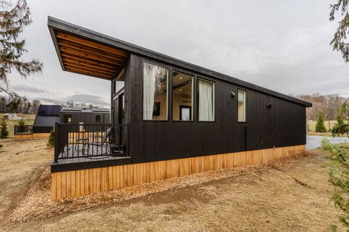 Black modern cabin exterior with covered deck, cedar skirting and large picture windows