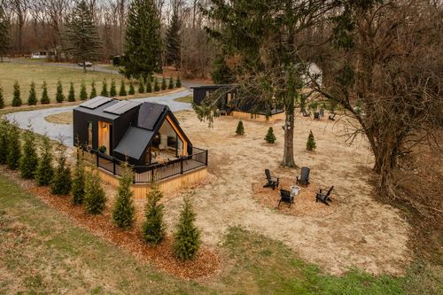 Aerial view of black A-frame cabins with fire pit seating nestled among evergreen trees