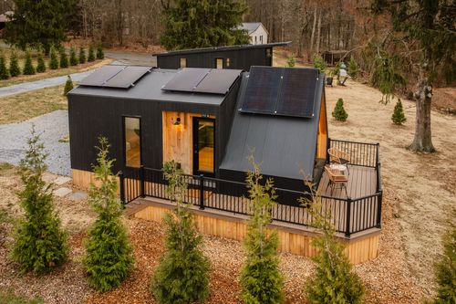 Aerial close view of a black cabin with rooftop solar panels and a covered deck
