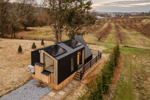 Aerial view of an A-frame cabin with solar panels overlooking a dormant orchard