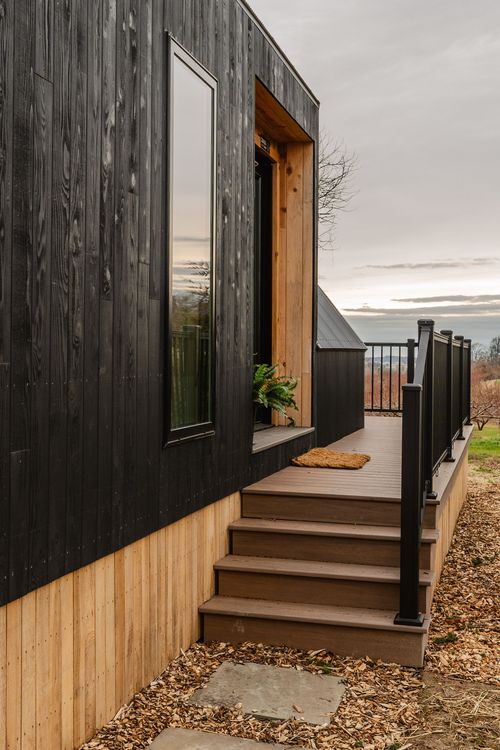 Close view of a black cabin's cedar-trimmed entry door and covered deck railing