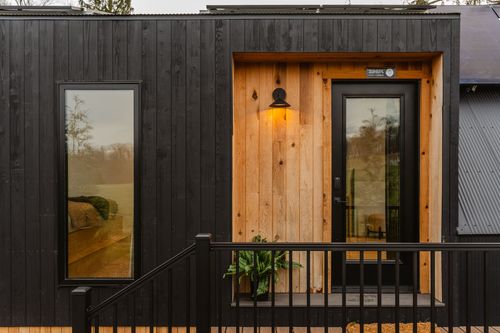 Cabin entry with cedar door surround, sconce lighting and black metal railing