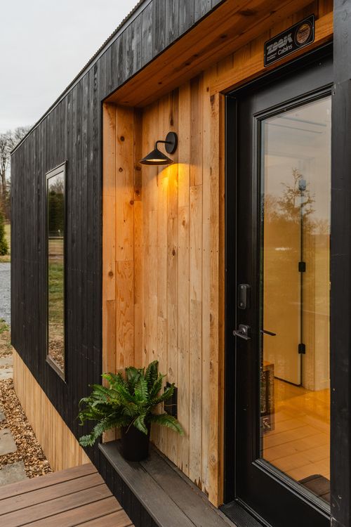 Close view of a cabin's cedar entry door surround with sconce light and potted fern