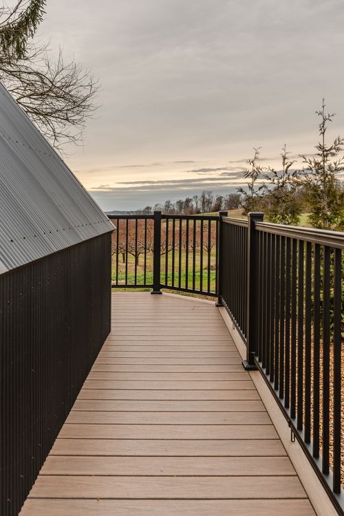 Elevated wood walkway with black metal railing connecting to a deck overlooking an orchard