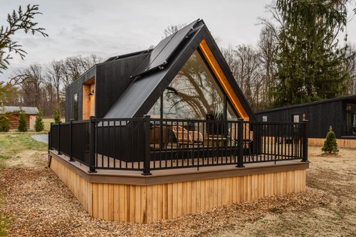 Black A-frame cabin exterior with rooftop solar panels and a covered deck