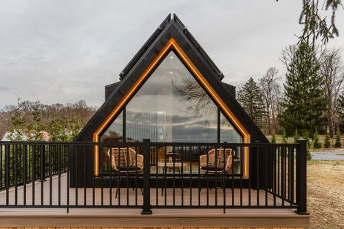 A-frame cabin gable with glowing amber trim and floor-to-ceiling glass above deck seating
