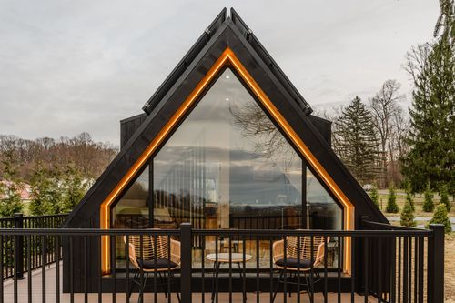 A-frame cabin gable close-up with amber LED trim framing a glass wall at dusk