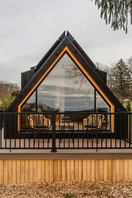 A-frame cabin gable with amber-lit trim, glass wall and wicker deck chairs