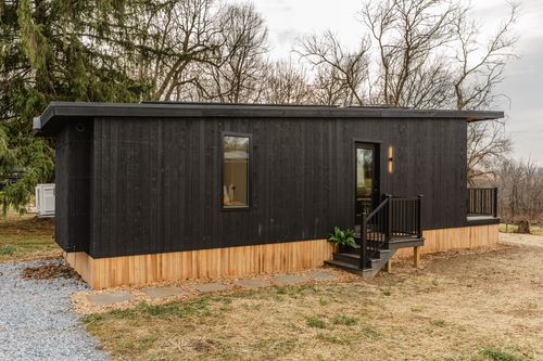 Black modern cabin exterior with covered deck, glass door and cedar wood skirting